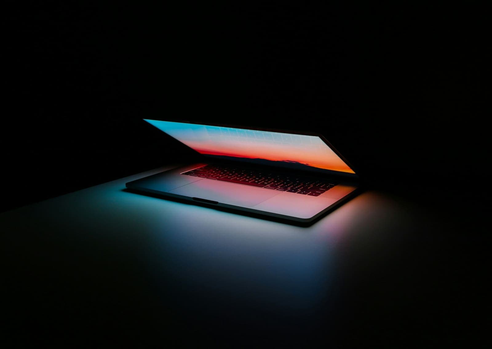 A laptop opening with colourful light in the dark